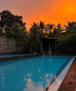 a blue swimming pool with a sunset in the background at Radawana Wasala Nature Resort in Radawana