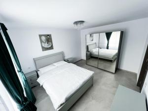 a white bedroom with a bed and a mirror at Casa Andreea in Curtea de Argeş