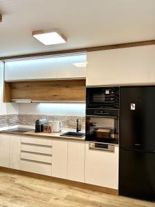 a kitchen with white cabinets and a black refrigerator at Apartman Lux-besplatno korišćenje zasebne garaže in Sremska Mitrovica