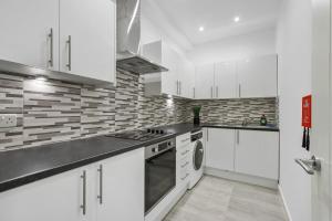 a white kitchen with white cabinets and a stove at Heathrow Airport Studios with En-Suite in Southall