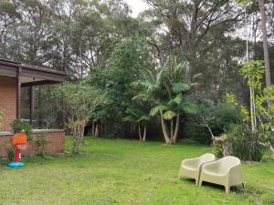 une cour avec deux chaises blanches dans l'herbe dans l'établissement Macyland, à Woollamia