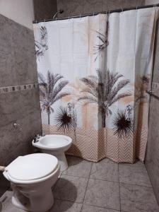 a bathroom with a toilet and a shower curtain with palm trees at Hospedaje Resiliencia in Cordoba