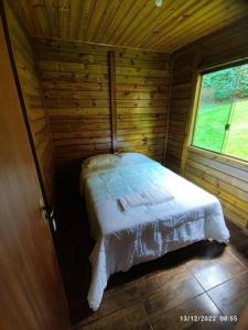 een bed in een houten hut met een raam bij Chalés Maravilha 01 in Alfredo Chaves