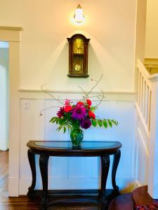 a vase of flowers on a table with a clock at Green Villa in Shaughnessy - Free Parking - Pet-Friendly in Vancouver