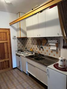 una cocina con armarios blancos y fregadero en Cozy Mountain Apartment with Cimone view, en Faidello