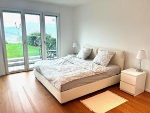 a white bedroom with a bed and a large window at Modernes Apartment an Traumlage in Lugano mit Seesicht in Paradiso