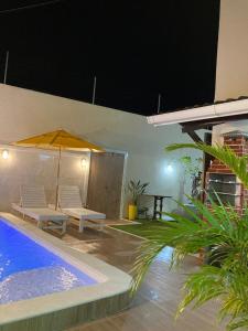a patio with two chairs and an umbrella next to a pool at Casa Brisas Arembepe - arejada e aconchegante - litoral norte da Bahia com crianca - WiFi in Arembepe