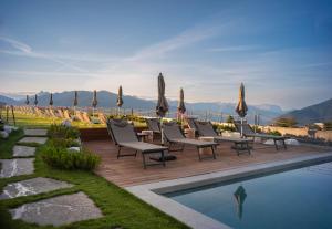 una terraza con sillas y sombrillas junto a una piscina en Familienhotel Familiamus en Maranza