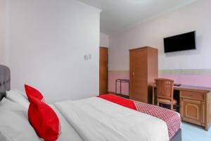 Schlafzimmer mit einem Bett mit roten Kissen und einem Schreibtisch in der Unterkunft OYO Life 90091 Wisma Pakuan Syariah in Bogor