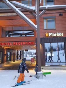 duas pessoas em esquis na neve em frente a um hotel em Ruka Park Base Camp em Ruka