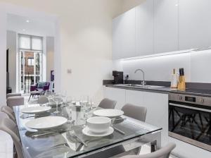a white kitchen with a table with plates and chairs at Harley Street Luxury Snug in London