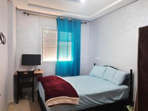 a bedroom with a bed with a desk and a blue curtain at Chambre calme et relaxante à centre ville Agadir in Agadir