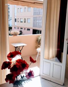 uma varanda com flores vermelhas e uma mesa e uma porta em La Victoire em Fréjus