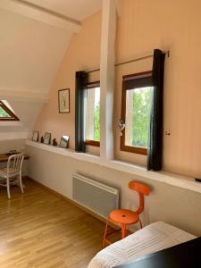 Habitación con 2 ventanas y silla naranja en Le Logis de la Chouette en Baugé