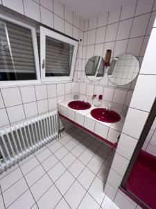 La salle de bains est pourvue de carrelage blanc, de deux lavabos et de miroirs. dans l'établissement Business Apartment Bühl, à Buhl