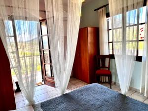 1 dormitorio con cortinas blancas, 1 cama y ventanas en Sunny house at ancient Mycenae, close to Nafplio! en Mykines