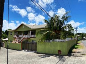 a green house with a fence and a palm tree at Casa Villa Apartments in Calliaqua