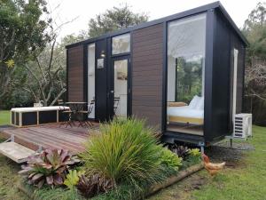 ein schwarzes winziges Haus in einem Garten mit einer Terrasse in der Unterkunft Creekside at Kuaotunu in Matarangi