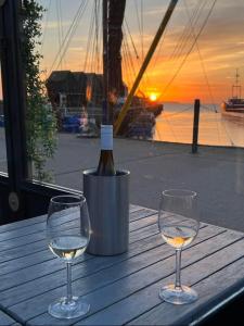 two wine glasses on a wooden table with a bottle of wine at Whitstable serenity in Whitstable