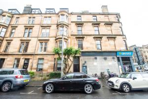 dos autos estacionados en un estacionamiento frente a un edificio en Two Bed Stylish Apartment in Heart of West End, en Glasgow