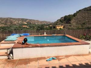 a woman is sitting next to a swimming pool at A tranquil mountain escape, casa particular, exclusive accommodation, private pool and terraces in Oria