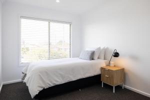 a white bedroom with a bed and a window at Coastal Breeze - 67 Burrill Street in Ulladulla