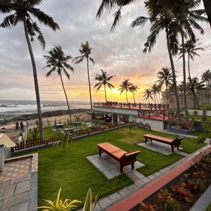 park z ławkami, palmami i oceanem w obiekcie Maadathil Beach Resort w mieście Varkala