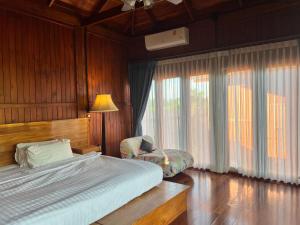 um quarto com uma cama, uma cadeira e janelas em Bann Rai I Na em Phrae