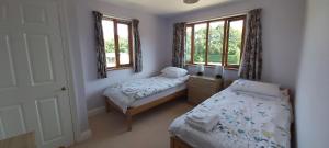 two beds in a room with two windows at Farmhouse: Beautiful rural location. London from 60 minutes. in Ashford
