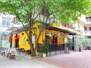 un bâtiment jaune avec des tables, des chaises et un arbre dans l'établissement Ngáo Home, à Hanoï