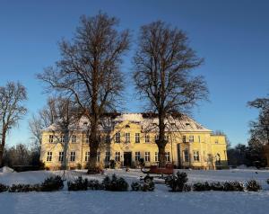 a large yellow building with trees in the snow at Gut Manderow an der Ostsee in Hohenkirchen
