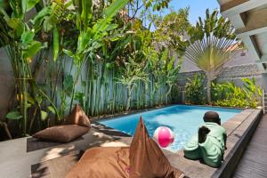 a swimming pool in a garden with a person sitting next to it at Balissimo Suites Seminyak by Betterplace in Seminyak