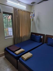 two beds in a room with blue sheets and a window at A & P Apartments in Thane
