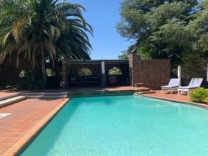 a swimming pool with two chairs and a palm tree at Footprints Self Catering Solar No Loadshedding in Lanseria