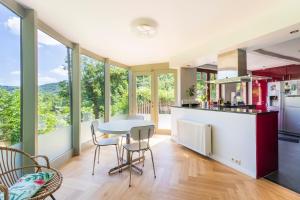 cocina con mesa, sillas y ventanas en Côté cour, côté source chambre d'hôtes, en Chaudfontaine