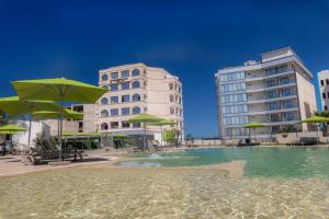 una piscina de agua con sombrillas y edificios verdes en BOUMERDES PLAZA Hôtel & Spa en Boumerdes