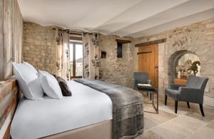 1 dormitorio con 1 cama blanca grande y pared de piedra en La Maison du Passage - Chambres - Suites premium, Spa, Piscine et Restaurant, en Martignargues