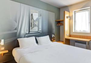 Un dormitorio con una gran cama blanca y una ventana en B&B HOTEL Dijon Les Portes du Sud, en Dijon
