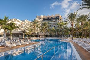 Una piscina con sillas y palmeras y un edificio. en Grupotel Orquidea, en San Agustín