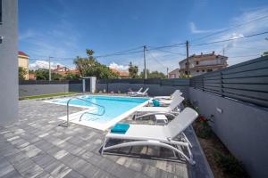 a swimming pool with white lounge chairs next to a fence at Modern villa Danica with pool in Zadar in Bibinje