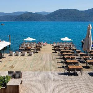 a dock with chairs and tables and umbrellas on the water at GÖKTÜRK OTEL in Muğla