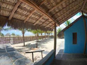 una cabaña en la playa con un banco bajo un techo de paja en Chalés Ventos de Amarração, en Ponta do Anel