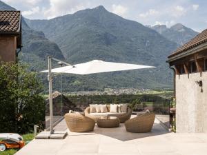 a patio with a white umbrella and chairs and mountains at Il Rustico Claro in Bellinzona