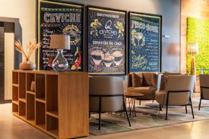 une salle d'attente avec une table, des chaises et des affiches dans l'établissement Novotel Curitiba Batel, à Curitiba