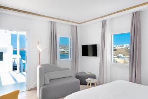 a white bedroom with a chair and a television at Cape Mykonos in Mýkonos City