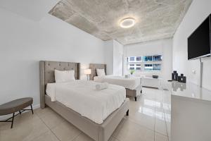 a white bedroom with two beds and a television at Spacious 3-Bedroom Midtown Condo in Miami