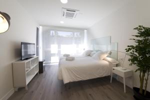 a white bedroom with a large bed and a tv at Pensión T5 Donostia Suites in San Sebastián