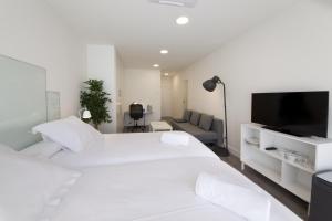 a white bedroom with two beds and a flat screen tv at Pensión T5 Donostia Suites in San Sebastián