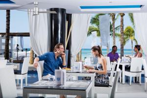 un homme et une femme assis à table dans un restaurant sur la plage dans l'établissement Riu Palace Jamaica - Adults Only - All Inclusive Elite Club, à Montego Bay