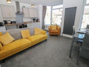 a living room with a yellow couch and a kitchen at Flat 2 Englehurst Mews in Buxton